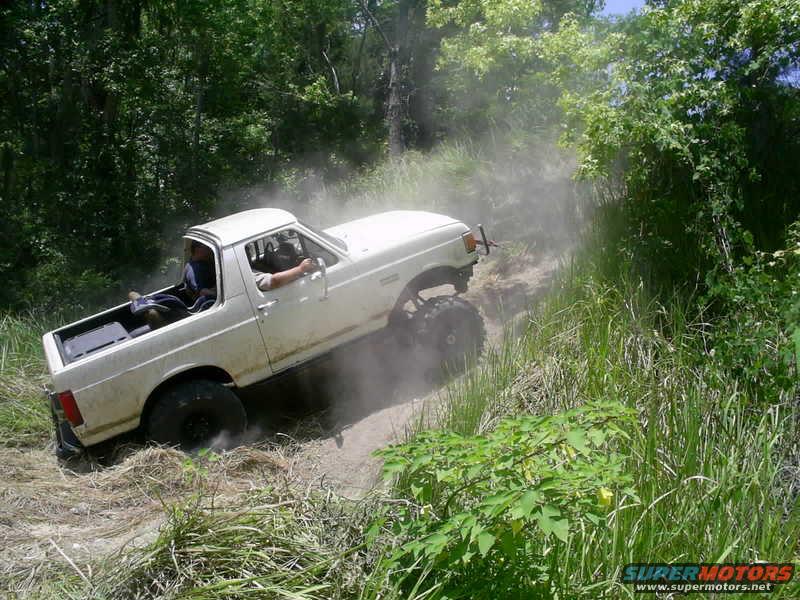 White 1987 Ford F-150 off-roading on a dirt path, kicking up dust