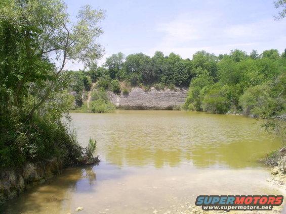 Water body with rocky shore and trees, Supermotors.net logo visible