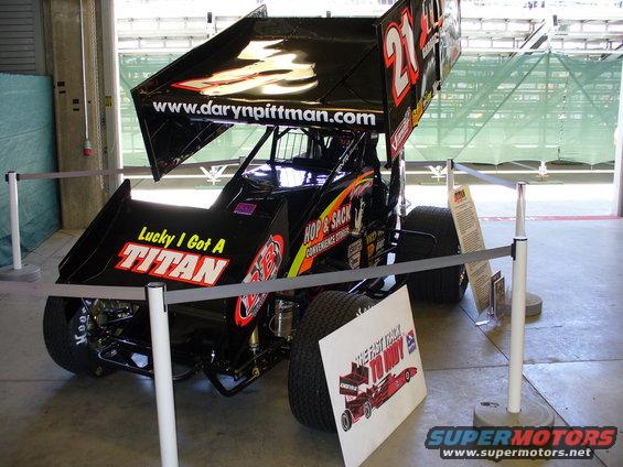Black sprint car with number 21 on the wing. Text on the car says 'Lucky I Got A TITAN' and 'HOP & SACK'
