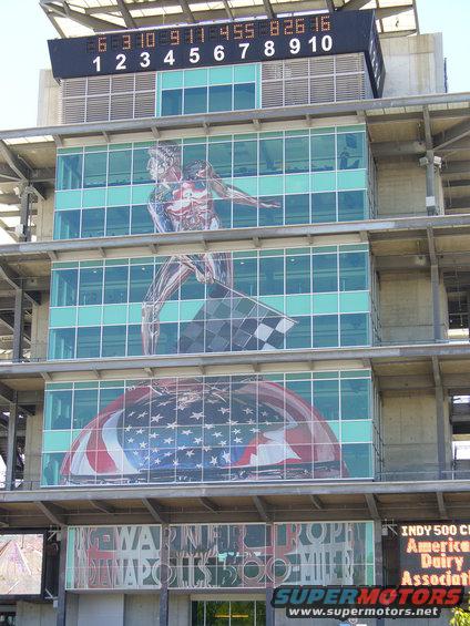 Scoreboard and murals on a building at the Indianapolis Motor Speedway, including a runner with a checkered flag and an American flag
