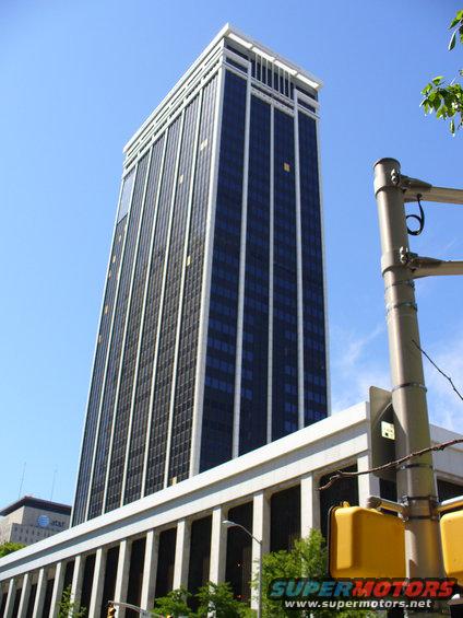 Tall office building with dark windows and white trim, seen from below. Traffic lights and a street sign are in the foreground