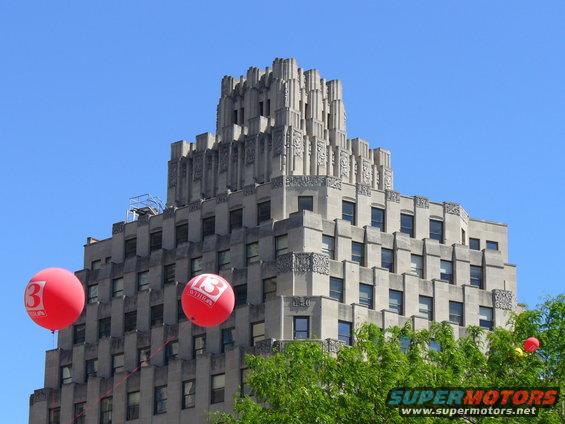 Art Deco building with two red balloons, one showing a '3' logo, against a blue sky