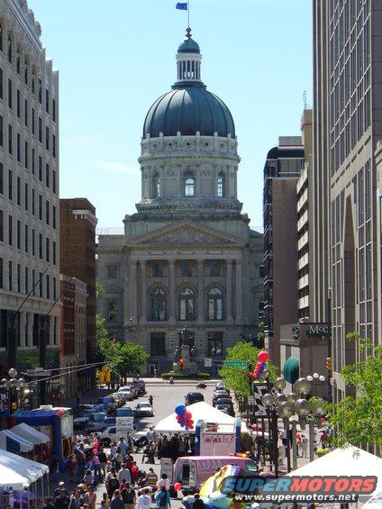Street scene with a large domed building, crowds of people, tents, and cars