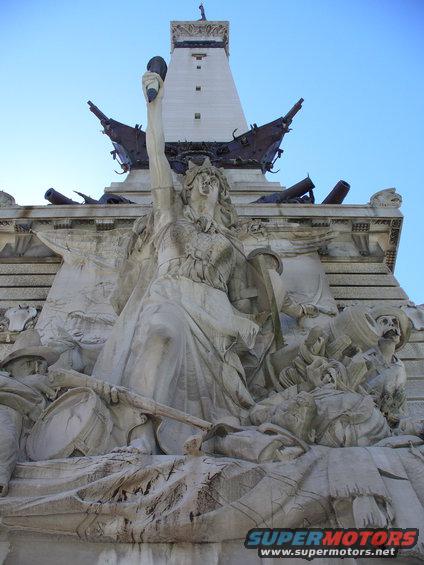 Monumental sculpture depicting figures, cannons, and a ship's prow against a blue sky