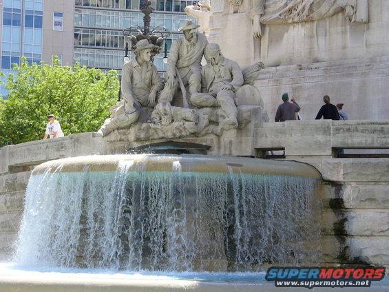 Fountain with statues of men, water flowing over the edge. Building in background