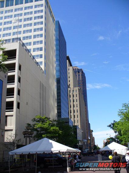 City street scene with tall buildings, white tents set up, and people walking