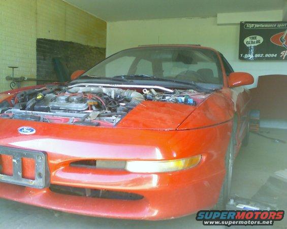 Red 1993 Ford Probe with hood open, showing engine bay. Parked in a garage with a "Supermotors.net" watermark