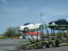 2007 Ford Mustang - A white convertible Mustang and a black pickup truck are being transported on a car carrier.