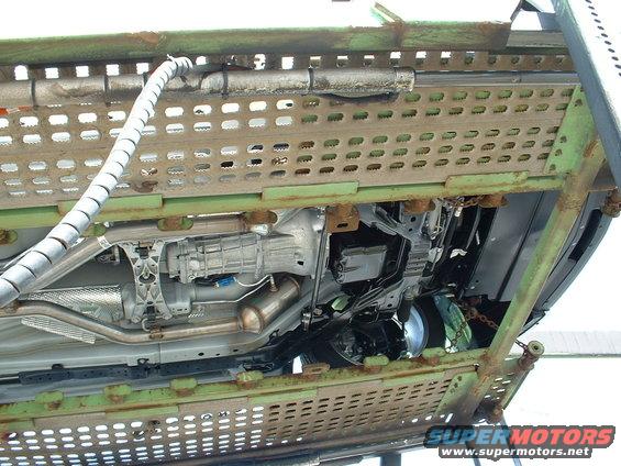 Undercarriage of a car on a green metal trailer, showing transmission, exhaust, and suspension components