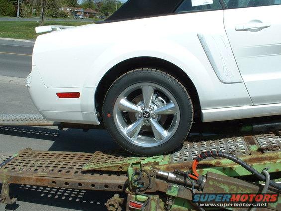White convertible car's rear quarter panel and wheel on a car carrier