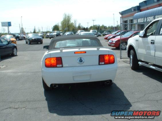 White convertible Mustang from rear, black top, dual exhaust, parked at dealership