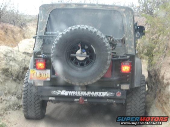 Black Jeep TJ with spare tire on rear, camouflage soft top, and "4 Wheel Parts" sticker on bumper
