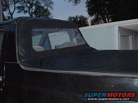 Black soft top on a black truck bed, showing part of the interior and a white building in the background