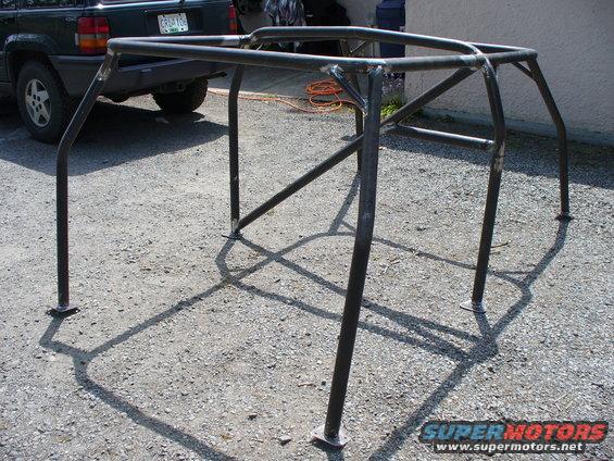 Custom roll cage frame on gravel, with a dark SUV in the background