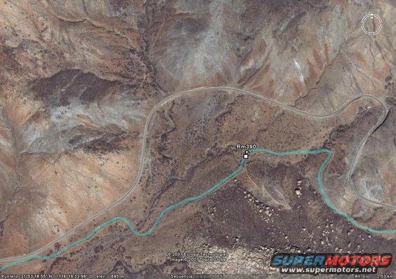 aerial view of a desert landscape with a winding road and a turquoise river, marked with 'Rm 390'