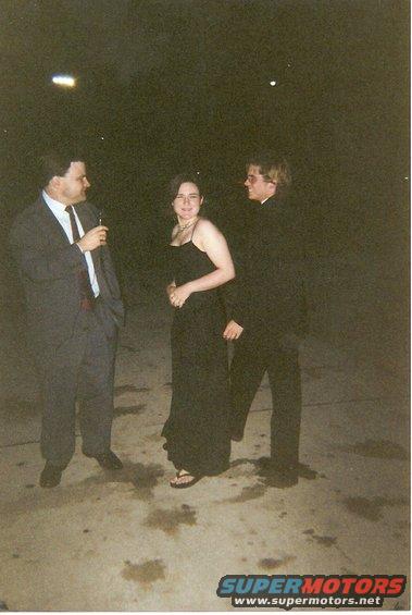 Three people in formal wear stand on a paved surface at night. A watermark reads www.supermotors.net
