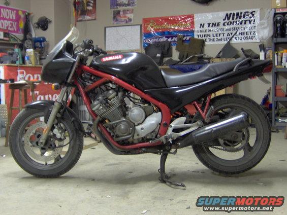Black Yamaha motorcycle with red frame parked in a garage. Text on the tank says YAMAHA