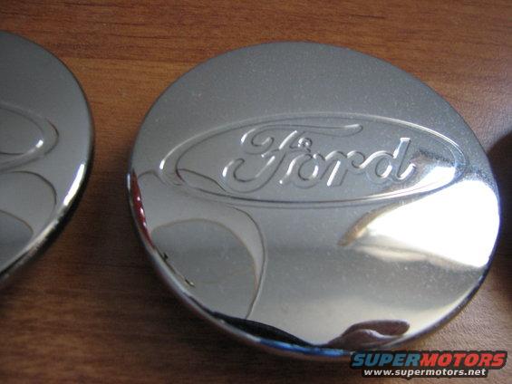 Chrome Ford hubcap with embossed logo on a wooden surface