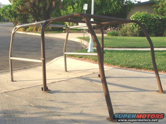 Rusty metal roll cage on a sidewalk, with a street and grass in the background
