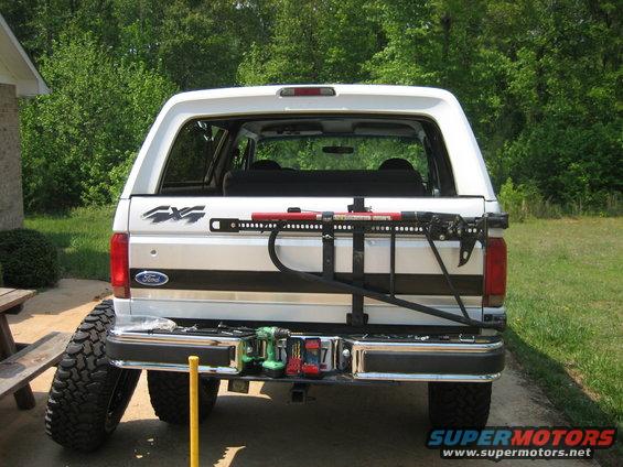 White Ford Bronco rear with a tire carrier holding a jack and tools, spare tire to the left
