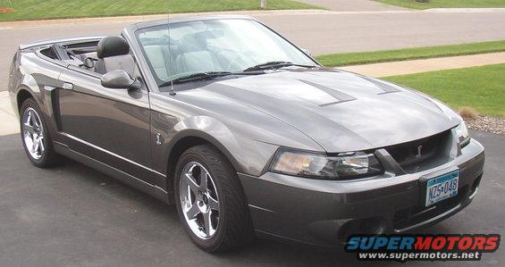 Gray Ford Mustang convertible with black top, chrome wheels, and racing stripes on the hood