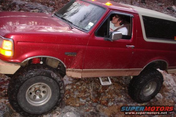 Red 1995 Ford Bronco with lifted suspension driving over rocks