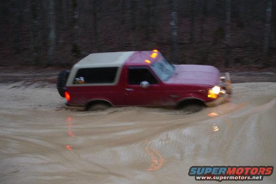 1995 Ford Bronco driving through muddy water, spare tire on rear