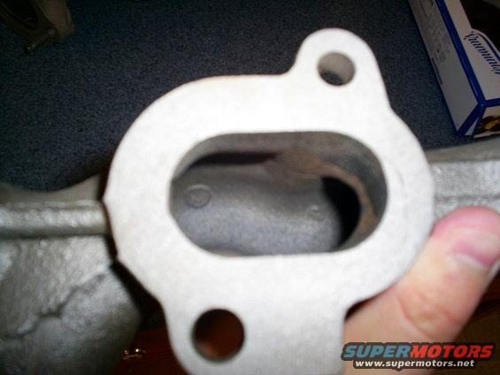 Exhaust manifold flange with two bolt holes and an oval opening, held by a hand