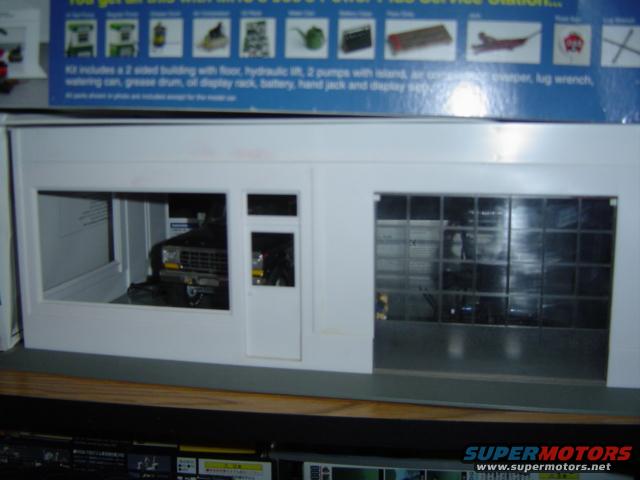 Model of a service station with a dark colored model car visible through the front window