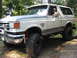 1990 Ford Bronco - A white Ford Bronco is shown off-road with a driver visible inside.