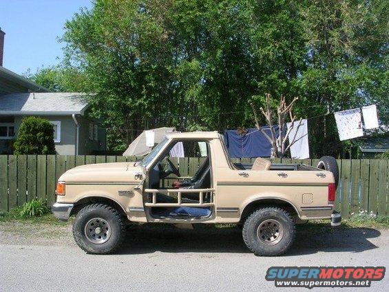 Tan Ford Bronco with doors removed, parked on a street
