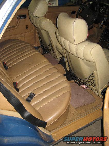 Tan leather seats and door panels inside a blue car. Seatbelts and seat pockets are visible