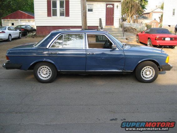 1982 Mercedes-Benz sedan parked on street, side view. Red convertible in background