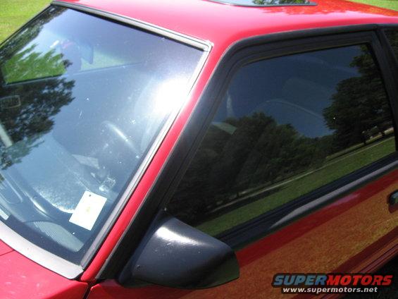 Red car side view, showing tinted windows and side mirror. A tag hangs from the rearview mirror