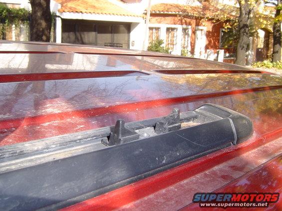 Close-up of a red SUV's roof rack and roofline. The rack appears to be missing a piece