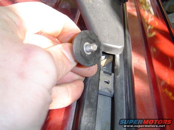Hand holding a rubber washer with screw near a red vehicle's window channel