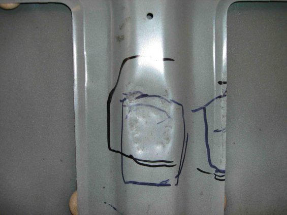 Close-up of a metal panel with blue marker lines drawn on it, possibly indicating a repair area