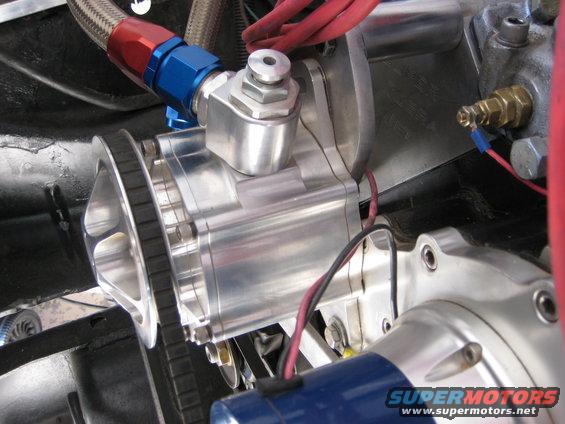 Close-up of polished aluminum engine component with a belt, braided hose, and wiring