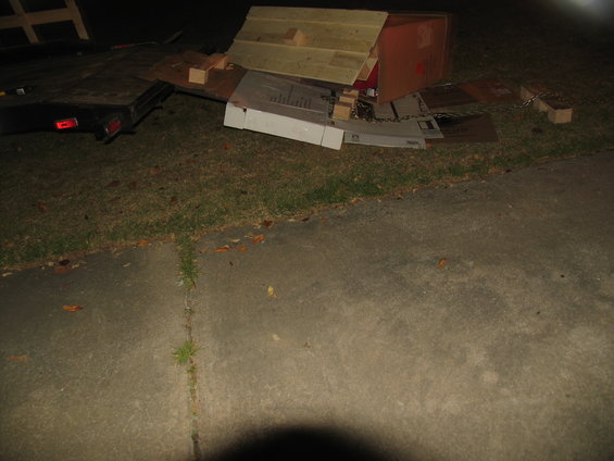Trailer with debris and a wooden structure on grass at night