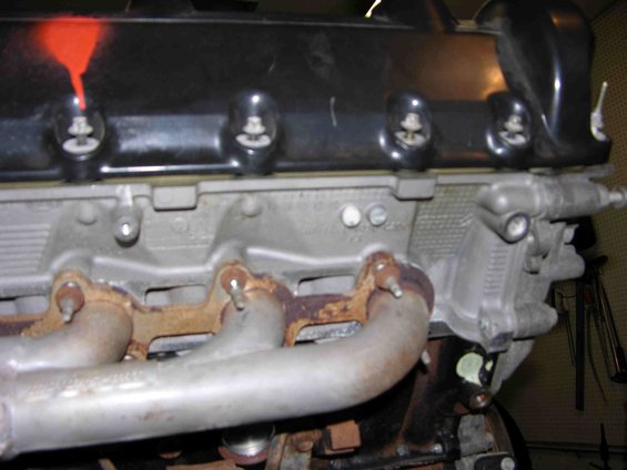Engine exhaust manifold with rust and red spray paint on black valve cover
