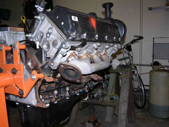 V8 engine on an orange engine stand, exhaust manifold visible
