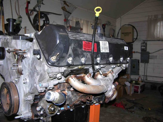 V8 engine on an orange stand in a garage, with tools on wall and electrical boxes in background