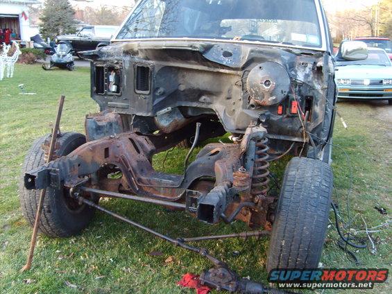 Truck chassis with front end removed, sitting on grass. Steering components are detached