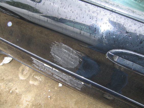 Black car door with scuff marks and damage near the handle