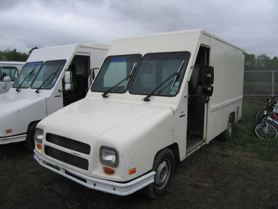 Two white step vans parked outdoors under a cloudy sky. The van in the foreground has its driver's door open
