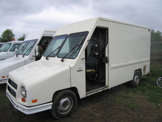 White step van parked next to other similar vans. Driver's side door is open