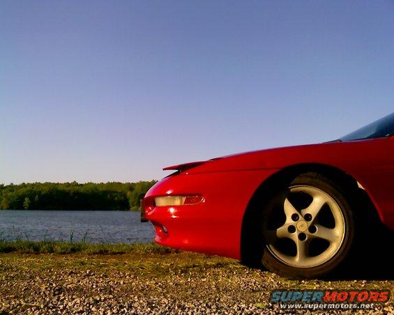 Red 1993 Ford Probe front quarter panel and wheel by a lake