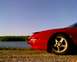 1993 Ford Probe - A red 1993 Ford Probe is parked by a lake, showing its front quarter panel and wheel.