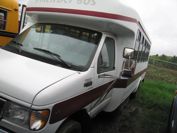White bus with maroon stripe and "FRIENDLY BUS" text, parked next to a yellow school bus