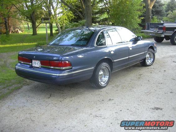 1996 Ford Crown Victoria sedan, blue, chrome wheels, parked on dirt road